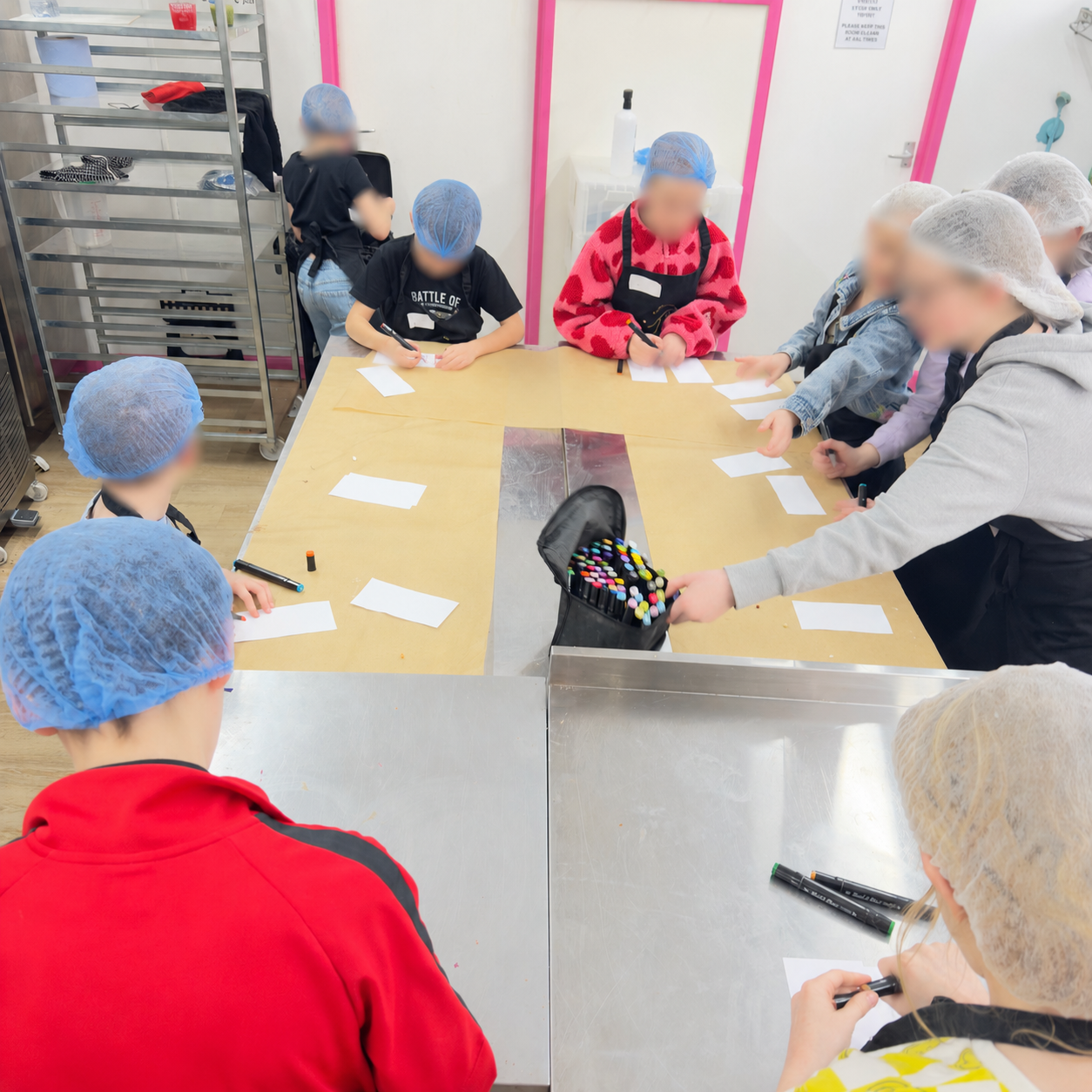 Group of children wearing hairnets around a table decorating chocolate bar wrappers