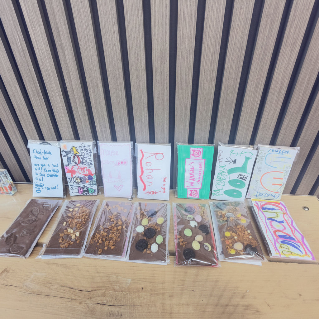 Assorted chocolate bars with colorful wrappers on a wooden surface against a striped wall.